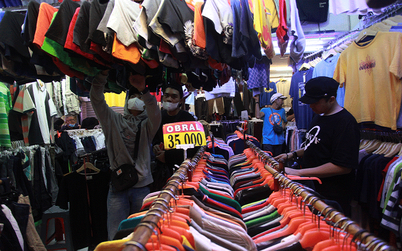 Second‑hand clothing vendor arranging leftover stock in shop